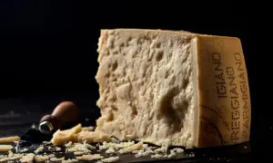 Kawałek parmezanu z widocznym napisem "Parmigiano Reggiano" i okruchy sera.