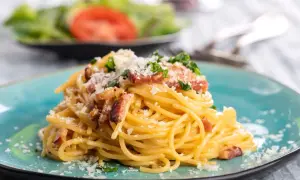 Talerz spaghetti carbonara z boczkiem i parmezanem, ozdobiony natką pietruszki.