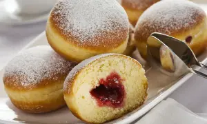 Pączki z dżemem posypane cukrem pudrem na białym talerzu.
