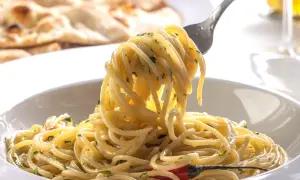 Widok z bliska na talerz spaghetti z widelcem unoszącym porcję makaronu, w tle płaski chleb.