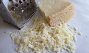 Tarka metalowa obok kawałka parmezanu i garści startego sera.