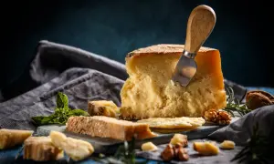 Kawałek twardego sera z nożem, bazylią i orzechami na niebieskim tle.
