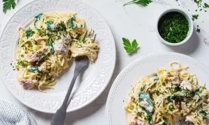 Dwa talerze spaghetti z tuńczykiem, szpinakiem i natką pietruszki.