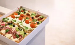 Pudełko z różnorodnymi, kolorowymi przekąskami typu bruschetta: z łososiem, pomidorkami, ogórkiem, rzodkiewką i wędliną.