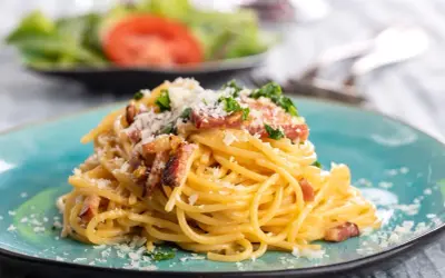 Talerz spaghetti carbonara z boczkiem i parmezanem, ozdobiony natką pietruszki.