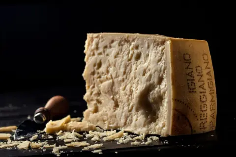 Kawałek parmezanu z widocznym napisem "Parmigiano Reggiano" i okruchy sera.