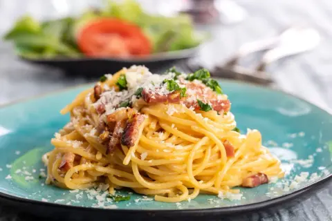 Talerz spaghetti carbonara z boczkiem i parmezanem, ozdobiony natką pietruszki.