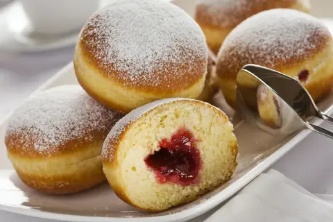 Pączki z dżemem posypane cukrem pudrem na białym talerzu.