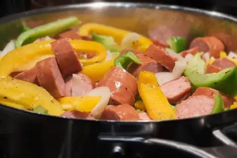 Kiełbasa z papryką i cebulą smażona na patelni.