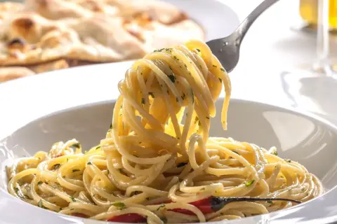Widok z bliska na talerz spaghetti z widelcem unoszącym porcję makaronu, w tle płaski chleb.