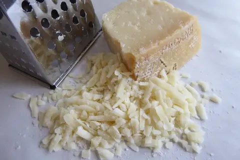 Tarka metalowa obok kawałka parmezanu i garści startego sera.