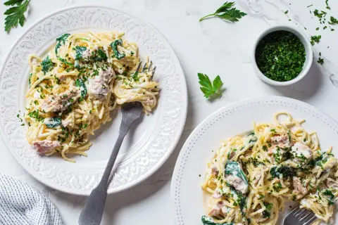 Dwa talerze spaghetti z tuńczykiem, szpinakiem i natką pietruszki.