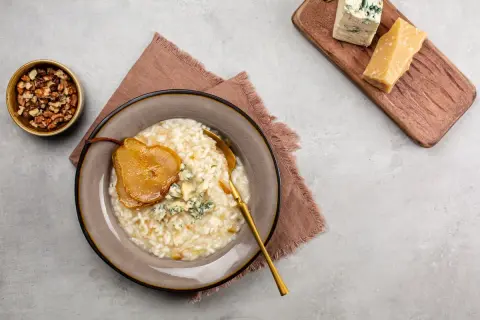 Risotto z gruszką i serem pleśniowym, obok orzechy i kawałki parmezanu.