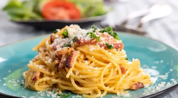 Talerz spaghetti carbonara z boczkiem i parmezanem, ozdobiony natką pietruszki.