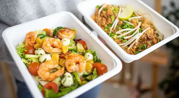 Dwa pojemniki z jedzeniem na wynos: sałatka z krewetkami i makaron Pad Thai.