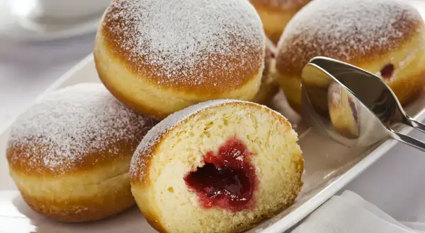 Pączki z dżemem posypane cukrem pudrem na białym talerzu.