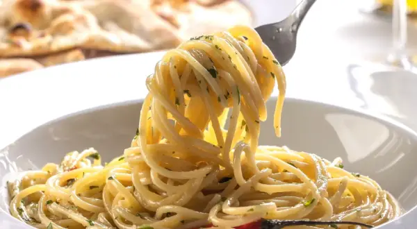 Widok z bliska na talerz spaghetti z widelcem unoszącym porcję makaronu, w tle płaski chleb.