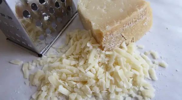 Tarka metalowa obok kawałka parmezanu i garści startego sera.