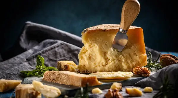 Kawałek twardego sera z nożem, bazylią i orzechami na niebieskim tle.