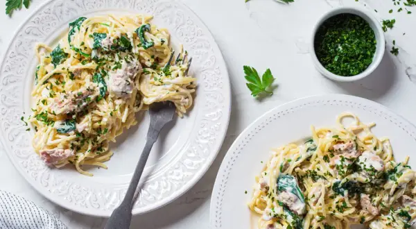 Dwa talerze spaghetti z tuńczykiem, szpinakiem i natką pietruszki.