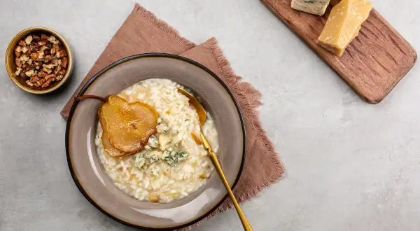 Risotto z gruszką i serem pleśniowym, obok orzechy i kawałki parmezanu.