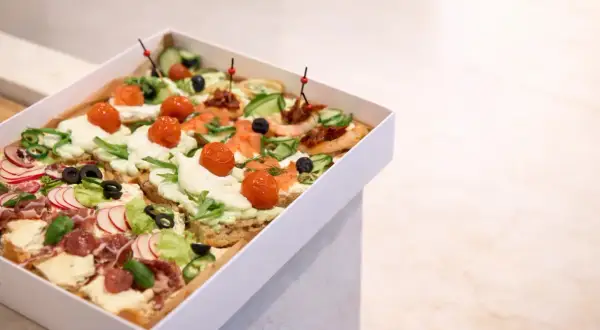 Pudełko z różnorodnymi, kolorowymi przekąskami typu bruschetta: z łososiem, pomidorkami, ogórkiem, rzodkiewką i wędliną.
