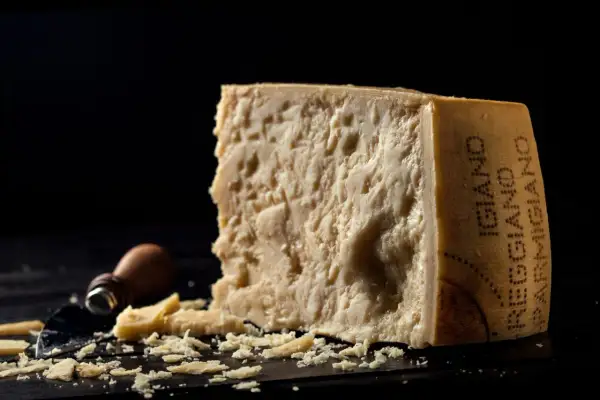 Kawałek parmezanu z widocznym napisem "Parmigiano Reggiano" i okruchy sera.