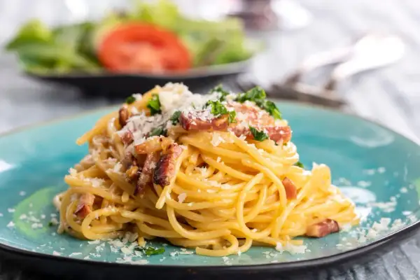 Talerz spaghetti carbonara z boczkiem i parmezanem, ozdobiony natką pietruszki.