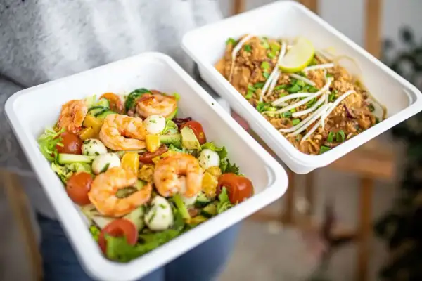 Dwa pojemniki z jedzeniem na wynos: sałatka z krewetkami i makaron Pad Thai.