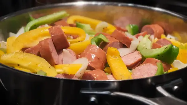 Kiełbasa z papryką i cebulą smażona na patelni.