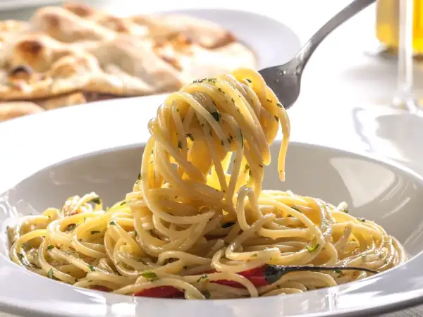 Widok z bliska na talerz spaghetti z widelcem unoszącym porcję makaronu, w tle płaski chleb.