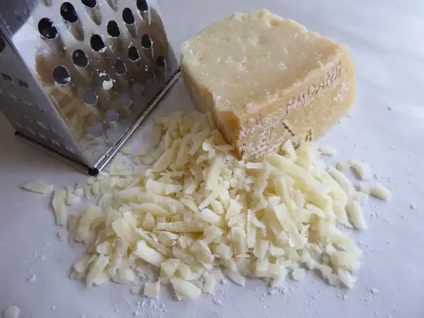 Tarka metalowa obok kawałka parmezanu i garści startego sera.