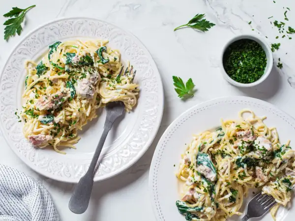 Dwa talerze spaghetti z tuńczykiem, szpinakiem i natką pietruszki.